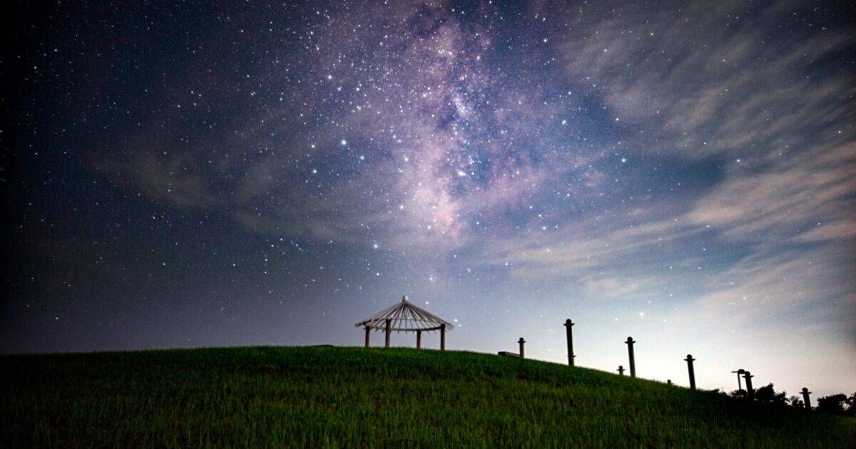 夜空に広がる天の川と草原の東屋