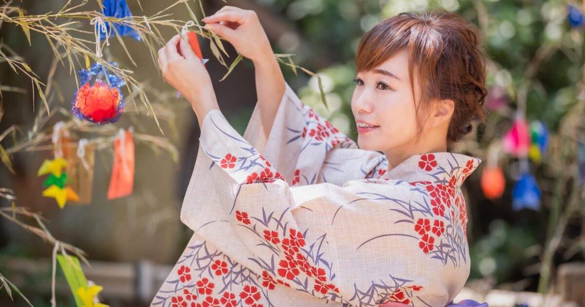 笹に七夕飾りを結ぶ笑顔の女性