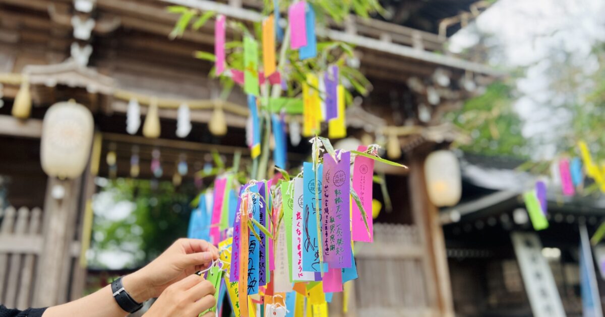 神社で短冊を結ぶ手と七夕の笹飾り